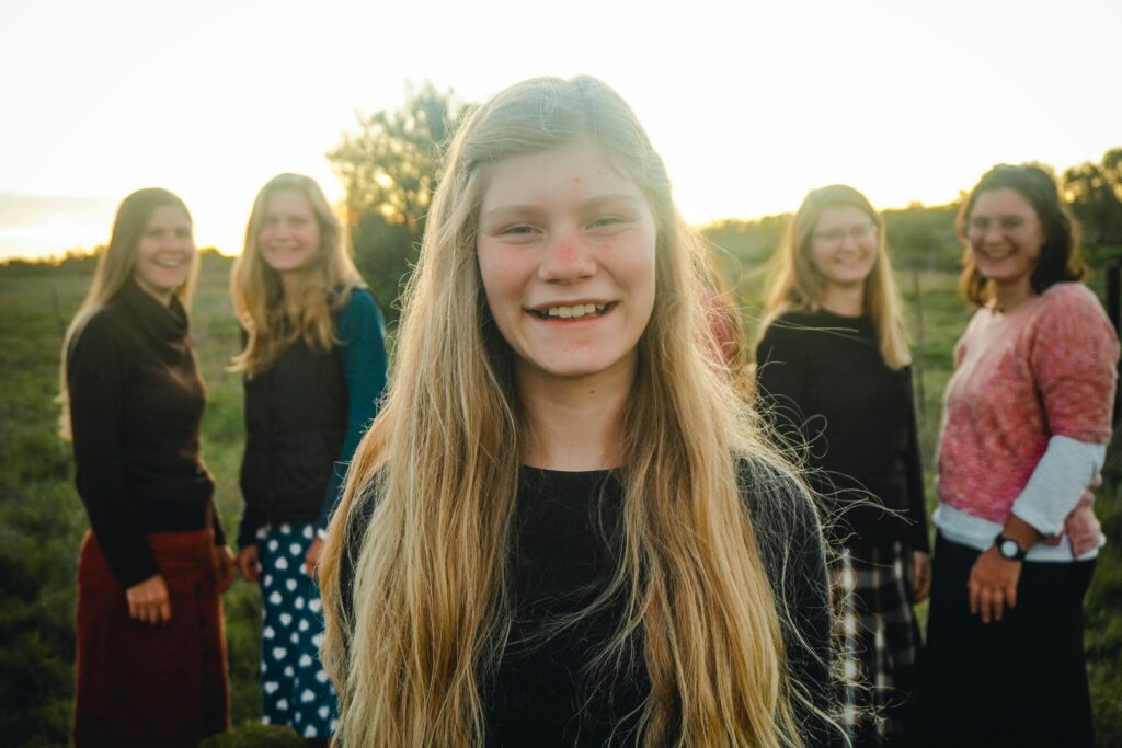 pexels-photo-37608890-37608890 Outdoor group portrait of smiling teenage girl with friends in a field during sunset.
