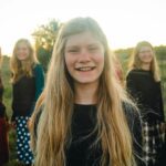 Outdoor group portrait of smiling teenage girl with friends in a field during sunset.